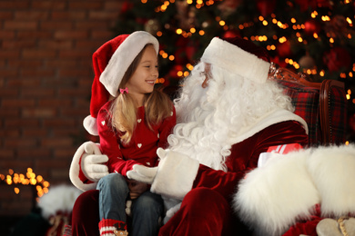 Photo of Santa Claus and little girl near Christmas tree indoors