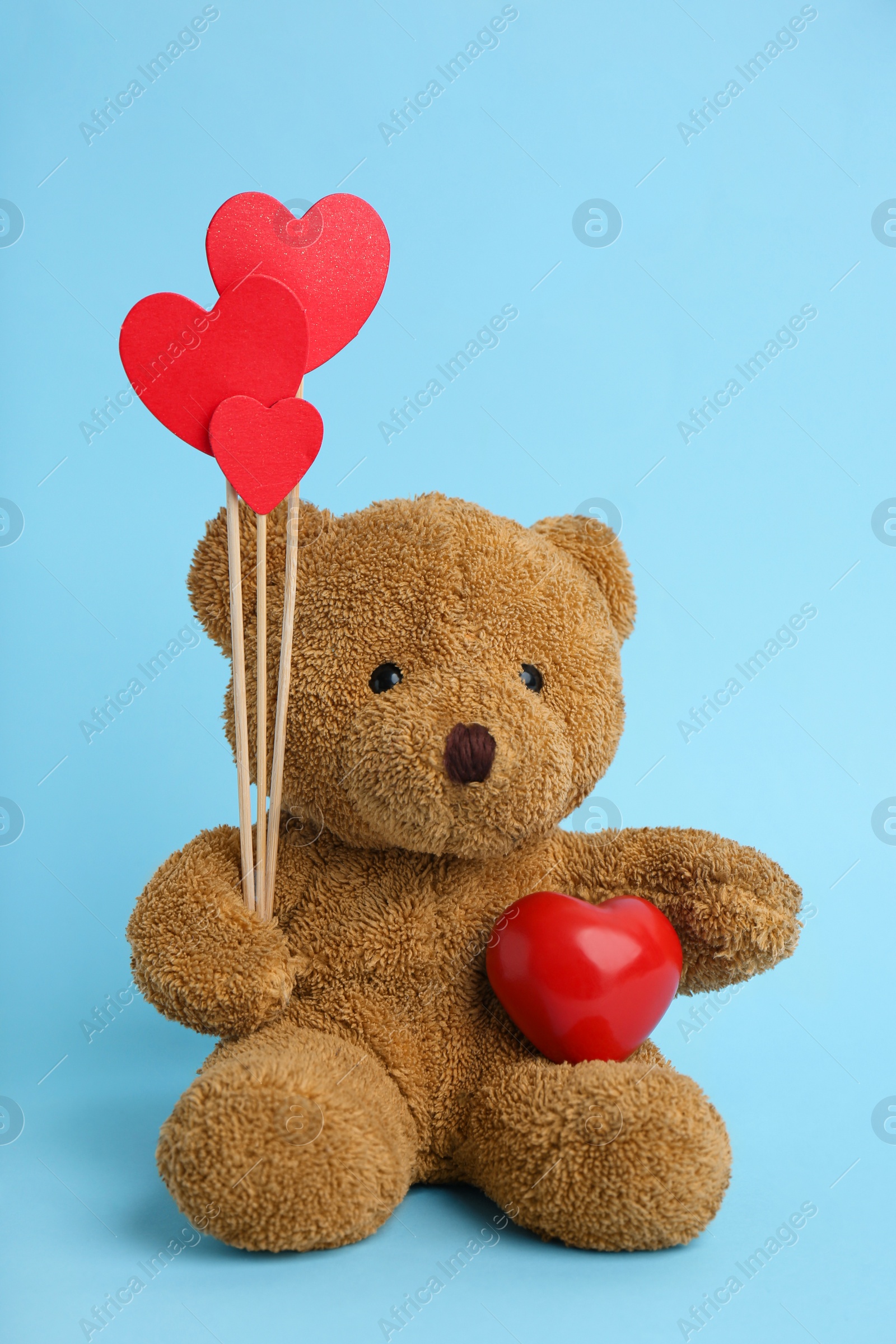Photo of Cute teddy bear with red hearts on light blue background. Valentine's day celebration