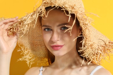 Beautiful young woman in straw hat on orange background