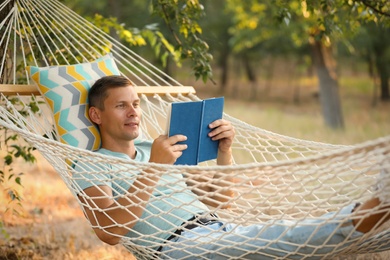 Man reading book in comfortable hammock at green garden