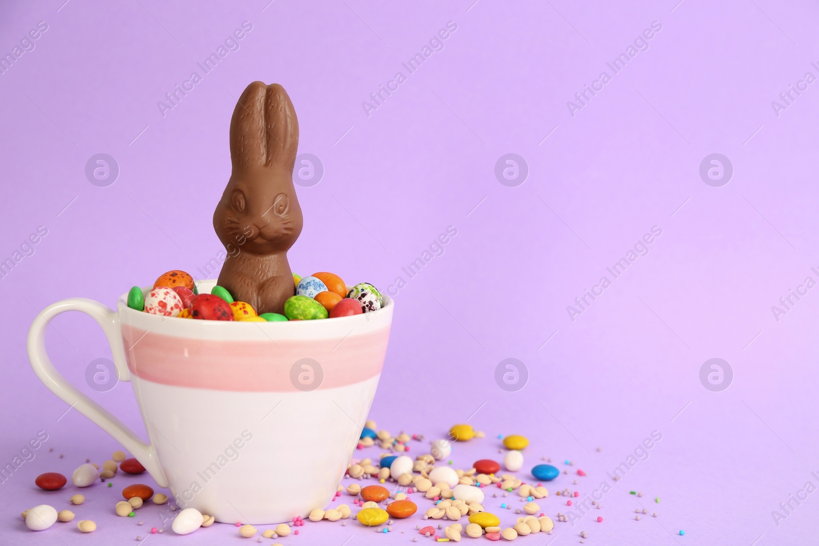 Photo of Chocolate Easter bunny and candies on lilac background. Space for text