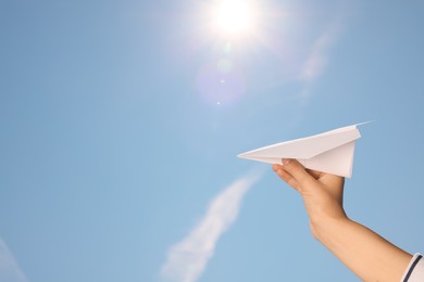 Photo of Woman holding paper plane against blue sky, closeup. Space for text