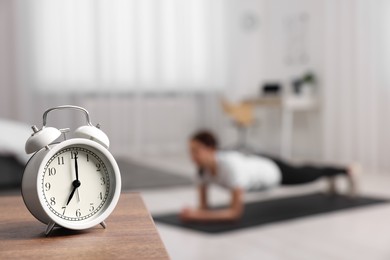 Morning routine. Alarm clock on wooden table and woman doing exercise, selective focus. Space for text