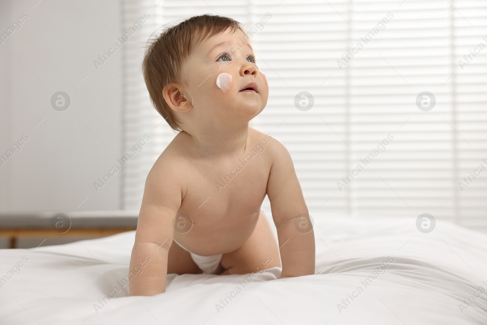 Photo of Cute little baby with moisturizing cream on face on bed at home