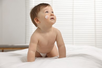 Cute little baby with moisturizing cream on face on bed at home