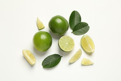 Photo of Whole and cut fresh ripe limes with green leaves on white background, flat lay