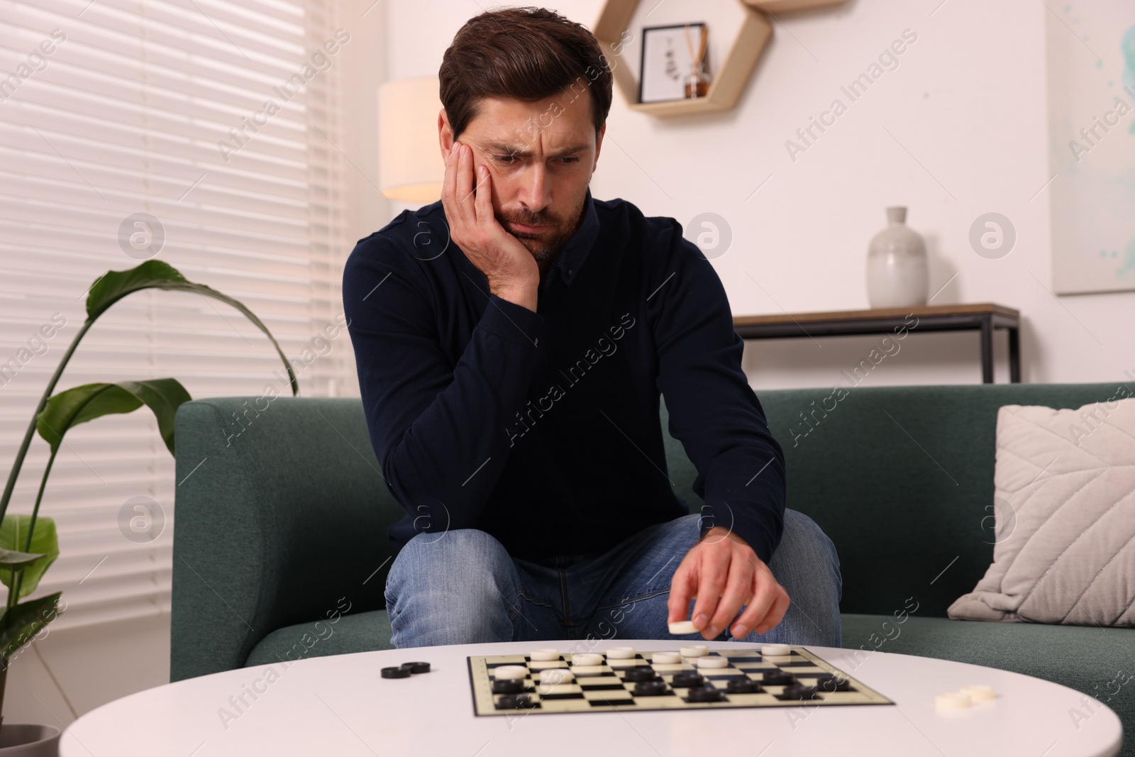 Photo of Thoughtful man playing checkers on sofa at home