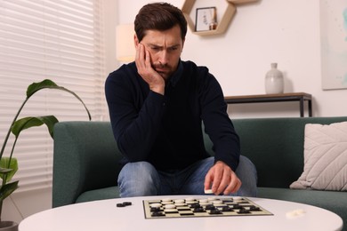 Thoughtful man playing checkers on sofa at home