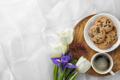 Photo of Delicious coffee, cookies and flowers on white cloth, flat lay. Space for text