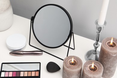 Dressing table with mirror, cosmetic products and burning candles in makeup room