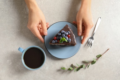 Photo of Woman with slice of chocolate sponge berry cake at table, top view