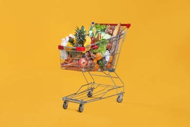 Photo of Shopping cart full of groceries on yellow background