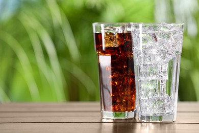 Photo of Glasses of different refreshing soda water with ice cubes on wooden table outdoors, space for text