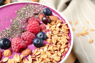 Delicious acai smoothie with berries and granola in bowl on table, closeup