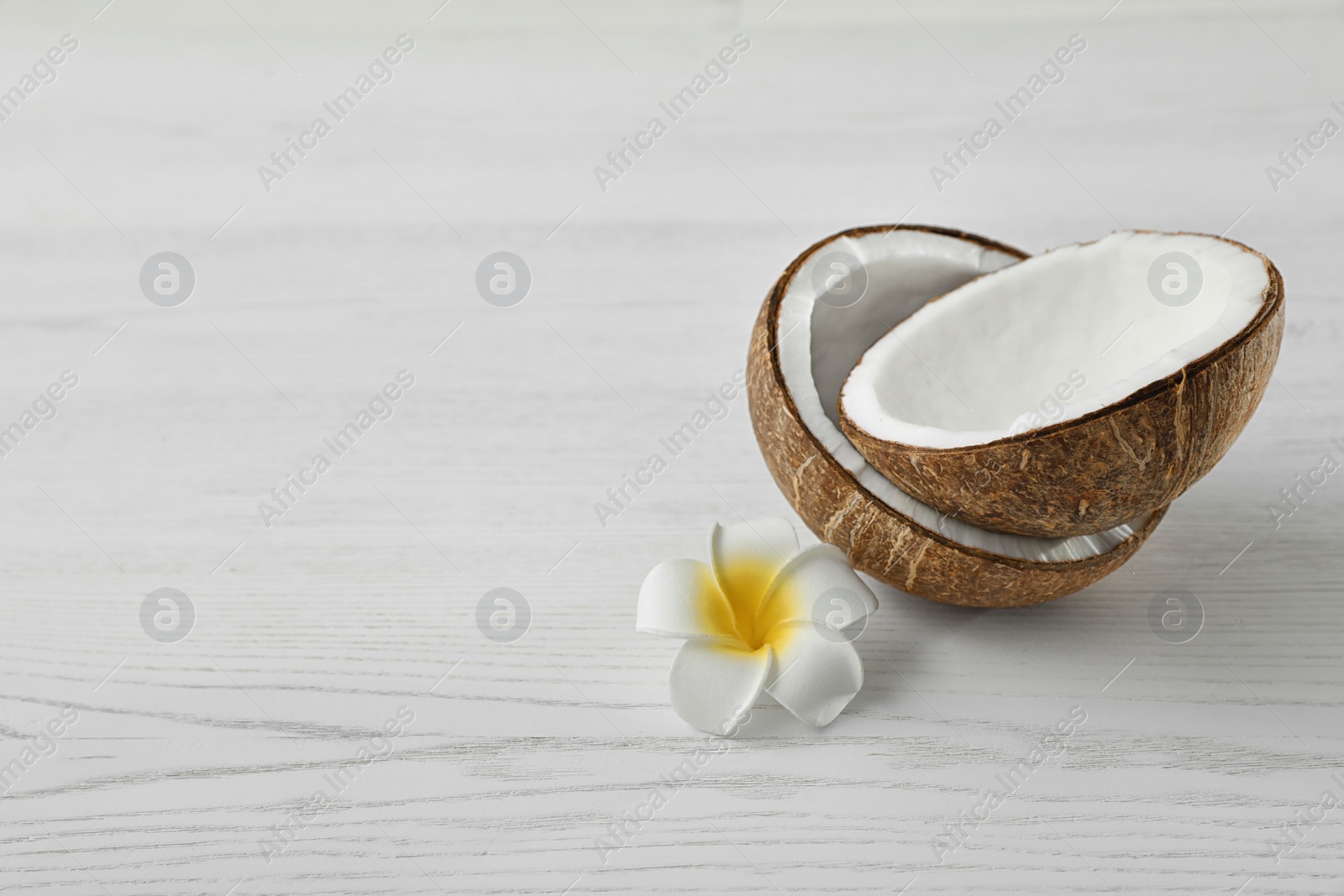 Photo of Halves of coconut and flower on white wooden background. Space for text