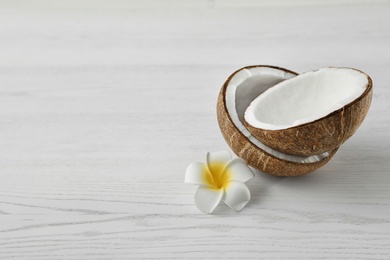 Photo of Halves of coconut and flower on white wooden background. Space for text