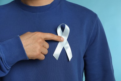 Photo of Man with ribbon on light blue background, closeup. Urology cancer awareness