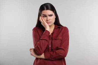 Sadness. Unhappy woman in red shirt on gray background