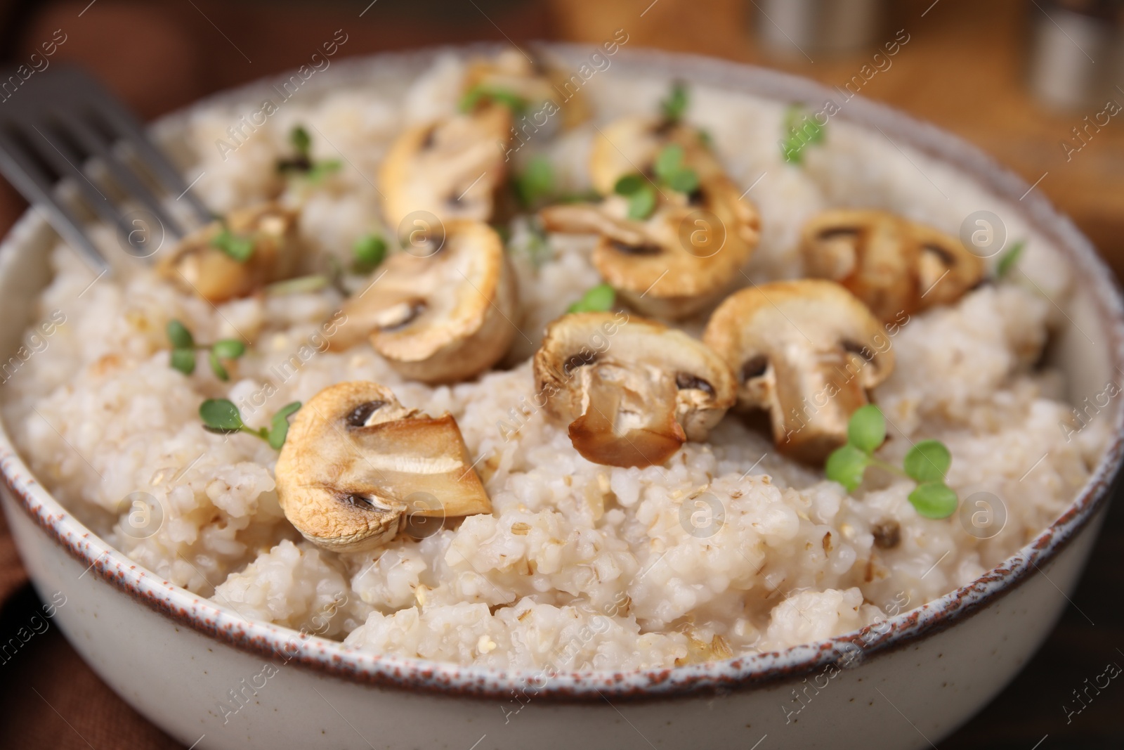 Photo of Delicious barley porridge with mushrooms and microgreens in bowl on table, closeup