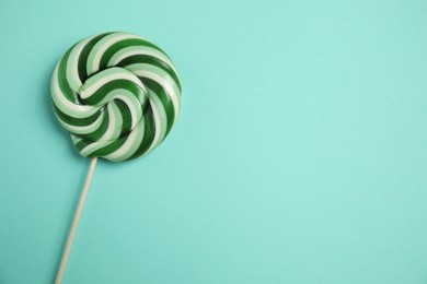 Photo of Stick with colorful lollipop swirl on turquoise background, top view. Space for text