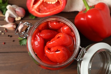 Glass jar with pickled peppers on wooden table, flat lay