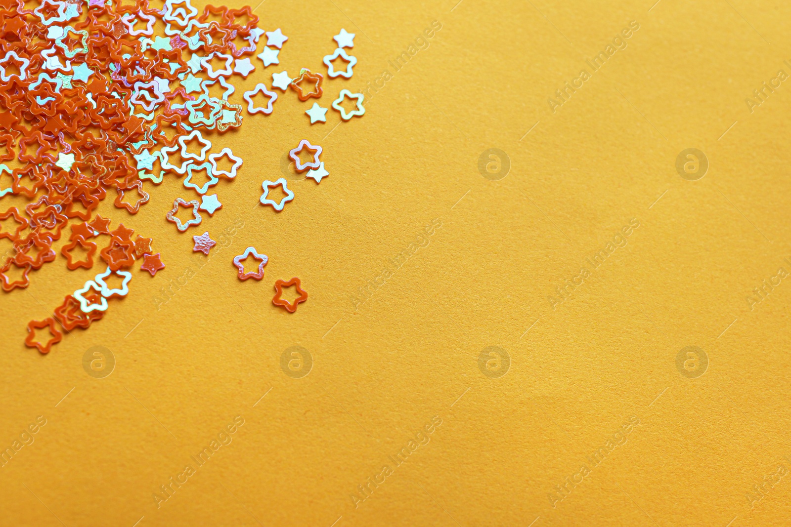 Photo of Shiny bright star shaped glitter on pale orange background. Space for text