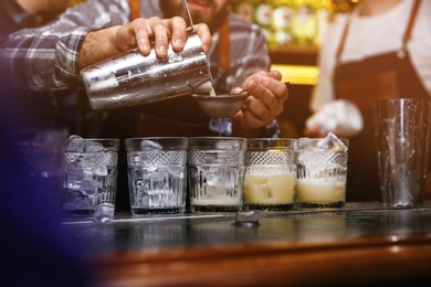 Photo of Bartender pouring tasty cocktail at table in nightclub, closeup