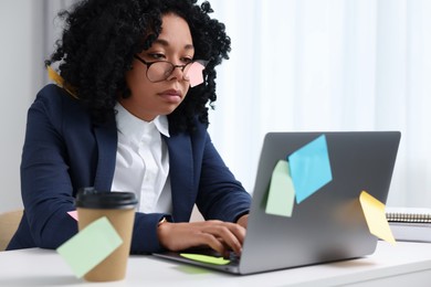 Deadline concept. Tired woman working with laptop in office. Many sticky notes everywhere as reminders