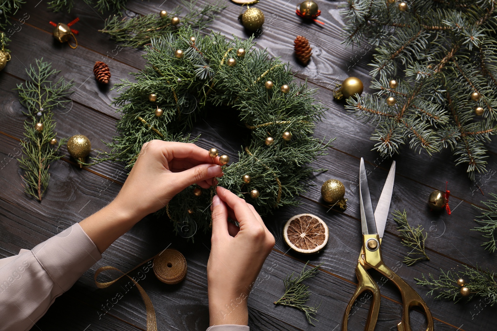 Photo of Florist making beautiful Christmas wreath at black wooden table, closeup