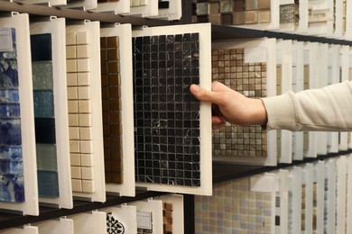 Photo of Man choosing tile among different samples in store, closeup