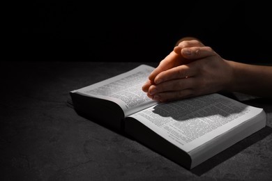 Religion. Christian woman praying over Bible at table against black background, closeup. Space for text