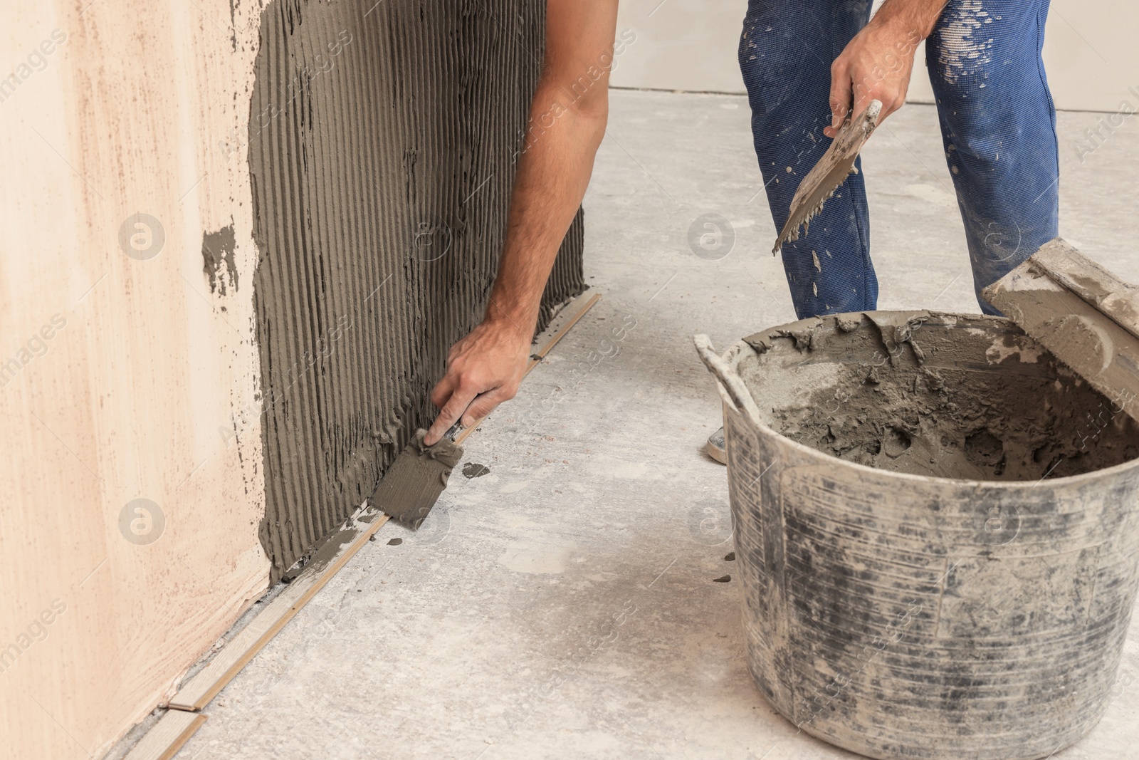 Photo of Worker spreading adhesive mix on wall for tile installation indoors, closeup