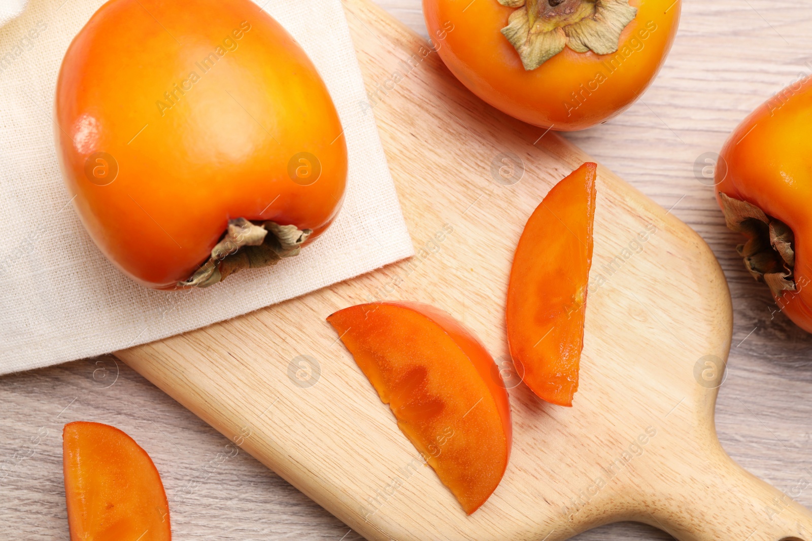 Photo of Delicious ripe persimmons on light wooden table, top view