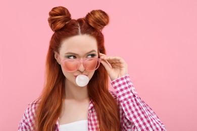 Photo of Beautiful woman with bright makeup blowing bubble gum on pink background