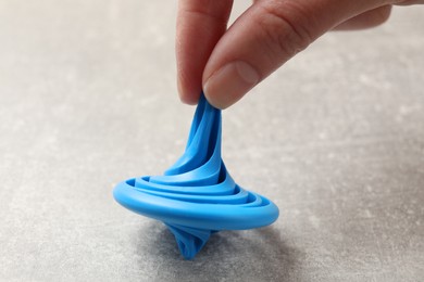 Photo of Woman playing with blue spinning top at grey textured background, closeup