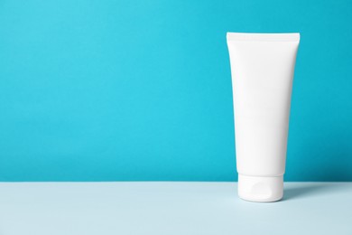 Tube of hand cream on table against light blue background, space for text