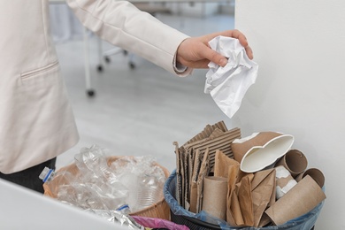 Photo of Woman putting crumpled paper into trash bin in office, closeup. Waste recycling