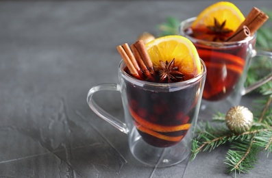 Photo of Glass cups with mulled wine and fir branches on grey table. Space for text