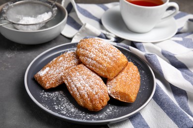 Photo of Delicious madeleine cakes with powdered sugar on grey table