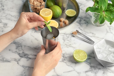 Photo of Young woman making delicious mint julep cocktail at table