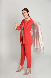 Young woman holding hanger with jacket on light grey background. Dry-cleaning service