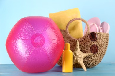 Photo of Pink inflatable ball and bag with beach accessories on light blue wooden table