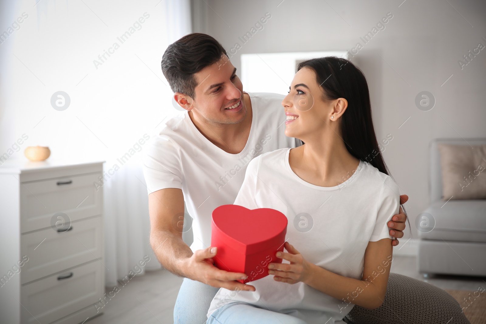 Photo of Man presenting gift to his beloved woman at home. Valentine's day celebration