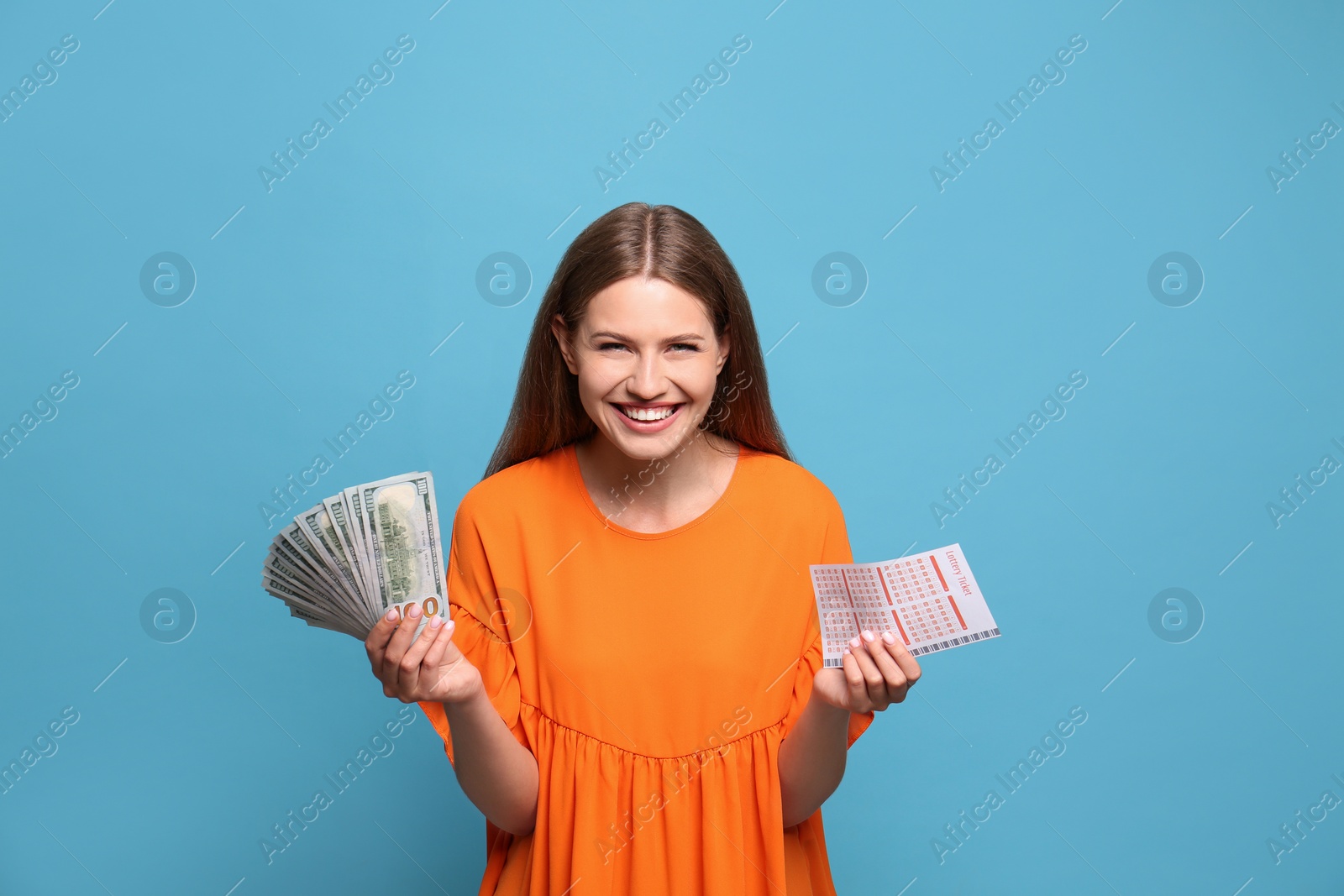 Photo of Portrait of happy young woman with lottery ticket and money fan on light blue background