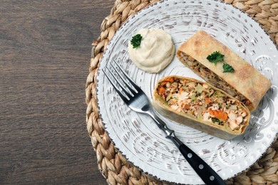 Pieces of delicious strudel with chicken, vegetables and sauce on wooden table, top view. Space for text