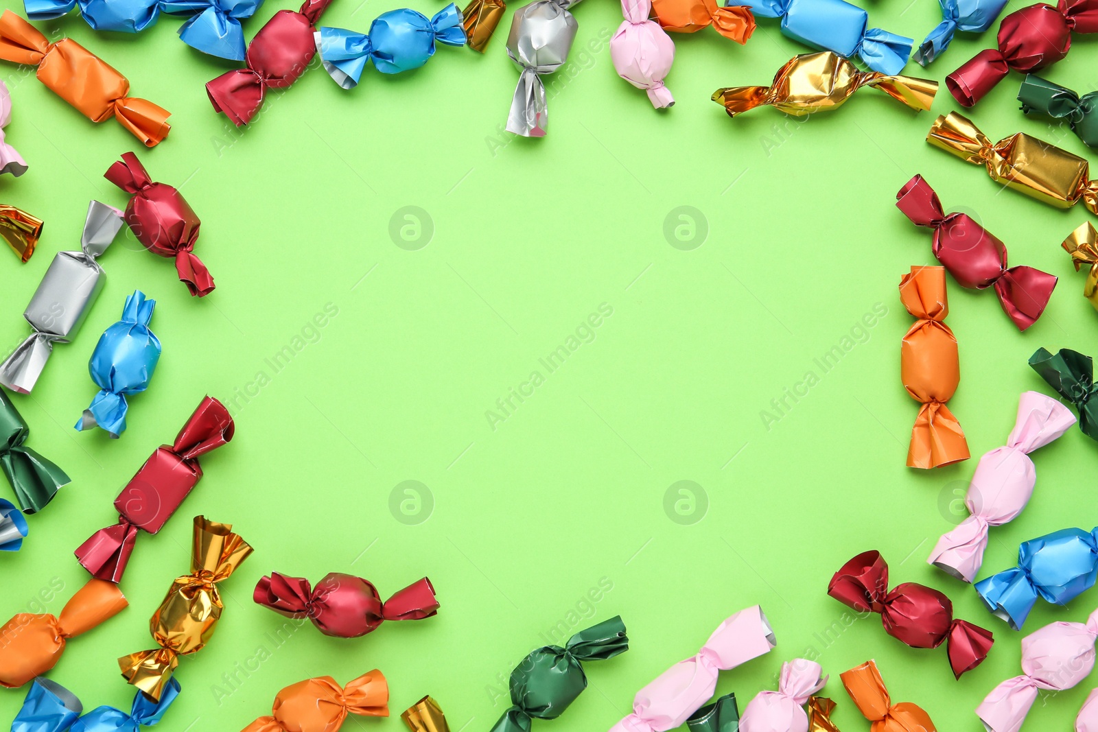 Photo of Frame of candies in colorful wrappers on light green background, flat lay. Space for text