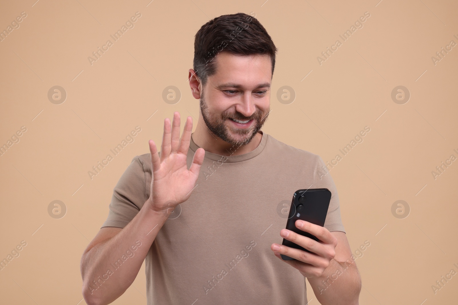 Photo of Happy man using smartphone and having video chat on beige background
