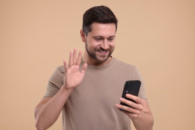 Happy man using smartphone and having video chat on beige background