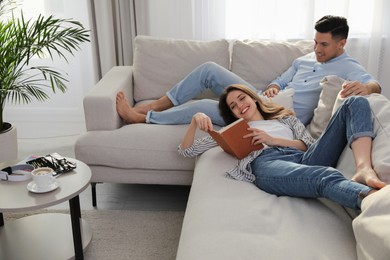 Photo of Happy couple with book on sofa in living room