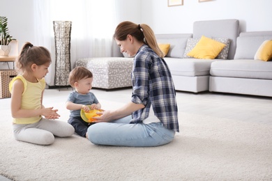 Photo of Mother with cute little children sitting on cozy carpet at home